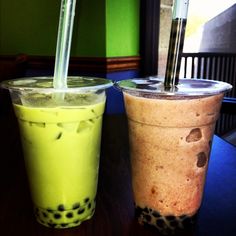 two drinks with straws sitting next to each other on a table in front of a window