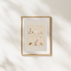 a white wall with a frame holding two cross - stitch rabbits and other animals on it