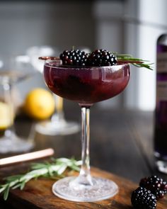 a close up of a wine glass on a table with berries in it and a bottle next to it