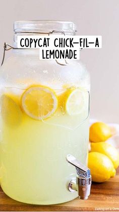 a glass jar filled with lemonade sitting on top of a wooden table next to sliced lemons