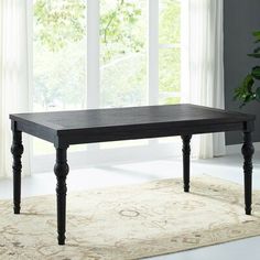 a black table sitting on top of a rug in front of a window with white curtains