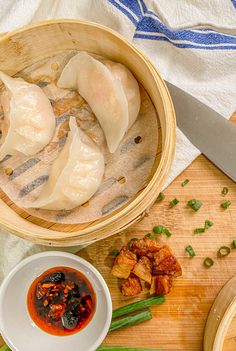 some dumplings are in a wooden bowl on a cutting board with chopsticks