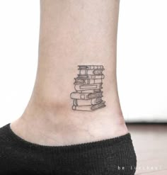 a small tattoo on the ankle of a woman's foot with books stacked up