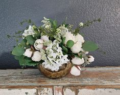 a vase filled with white flowers sitting on top of a wooden table next to a gray wall