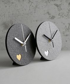 two clocks that have hearts on them sitting in front of a concrete wall and floor