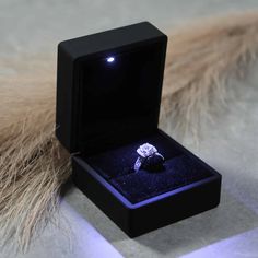 a diamond ring in a black box on top of some furry fur with the light shining through it