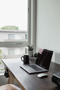 an open laptop computer sitting on top of a wooden desk next to a coffee mug