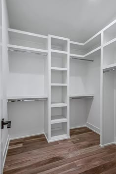 an empty walk in closet with white shelving and wood flooring on the side