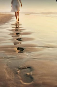 a woman walking on the beach with an umbrella over her head and footprints in the sand