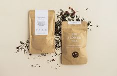 two bags of tea sitting next to each other on top of a white table with dried flowers