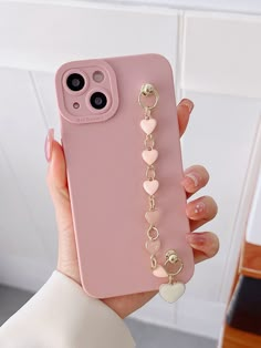 a person holding up a pink phone case with heart charms