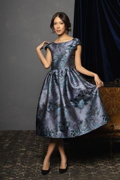 a woman standing in front of a couch wearing a dress with blue flowers on it