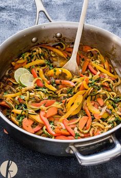 a pan filled with vegetable stir fry on top of a table next to a wooden spoon