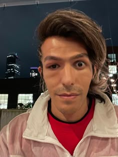 a man with long hair wearing a red shirt and white jacket looking at the camera