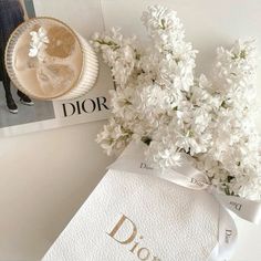 white flowers are in a vase next to a dior brochure