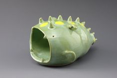 a green ceramic vase with spikes on it's head and yellow dots in the center