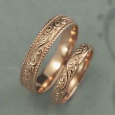 two gold wedding bands with intricate designs on each side, set against a gray background