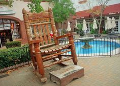 a wooden rocking chair sitting next to a swimming pool in front of a storefront