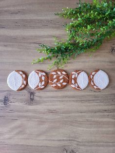 four cookies decorated with white and brown designs on top of a wooden table next to a potted plant