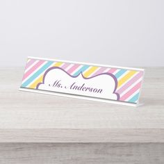 a colorful striped name plate on a white wooden table with a pink, blue, yellow and green stripe background