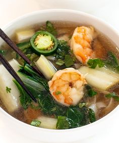 a white bowl filled with soup and vegetables next to chopsticks on the side