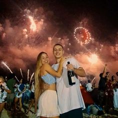 a man and woman standing next to each other with fireworks in the sky behind them