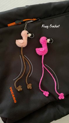 two crocheted flamingos hanging from a black bag