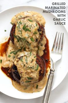 two stuffed mushrooms covered in gravy on a white plate with a fork next to it