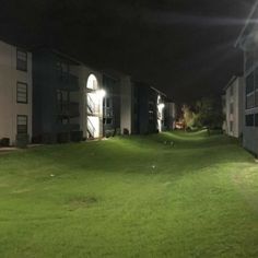 an apartment complex at night with lights shining on the lawn and green grass in front