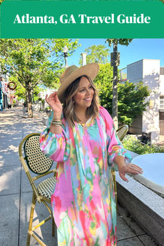 a woman in a colorful dress and hat standing on the sidewalk with her arms out