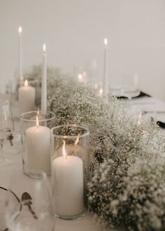 candles are lit on a table with white flowers and greenery