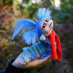 a hand holding a small stuffed animal with blue hair and red nose, in the palm of someone's hand