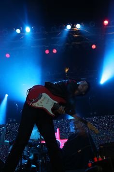 a man playing guitar on stage with blue and red lights in the backround