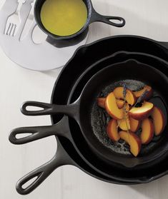 an iron skillet filled with sliced peaches on top of a white table next to utensils