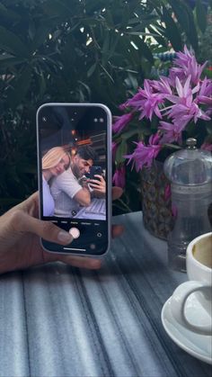 a person holding up a cell phone to take a selfie with flowers in the background