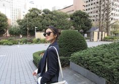 a woman walking down the street carrying a white purse in her hand and wearing sunglasses