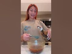 a woman is mixing something in a glass bowl with a whisk on it