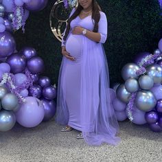 a pregnant woman standing in front of purple and silver balloons with her hands on her belly