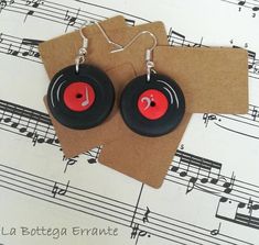 pair of black and red earrings with musical notes in the background on top of sheet music