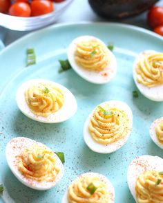 several deviled eggs on a blue plate with tomatoes and seasoning in the background