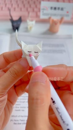 a person is holding a small origami cat with a pen in their hand