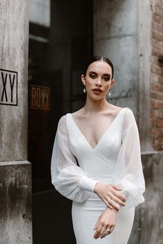 a woman wearing a white dress standing in front of a building with her hands on her hips