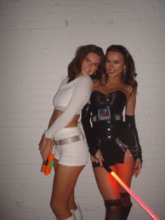 two women dressed up in costumes posing for a photo with lightsabes and swords