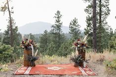 two vases filled with flowers sitting on top of a red rug in the woods