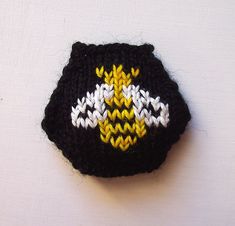 a crocheted black and yellow object on a white surface with one eyeball in the center