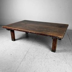 an old wooden table sitting on top of a white tile floor in front of a gray wall