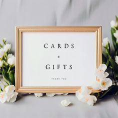 white flowers are next to a gold frame with words saying cards and gifts on it