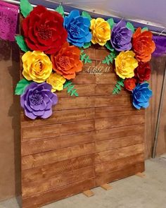 colorful paper flowers decorate the side of a wooden wall in front of a purple banner