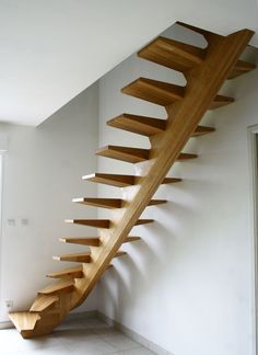 a wooden stair case in the corner of a room with white walls and tile flooring