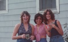 three women standing next to each other in front of a house holding cups and smiling